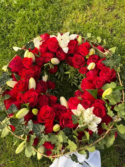 Trauerkranz aus roten Rosen mit weißen Lilien und Efeu